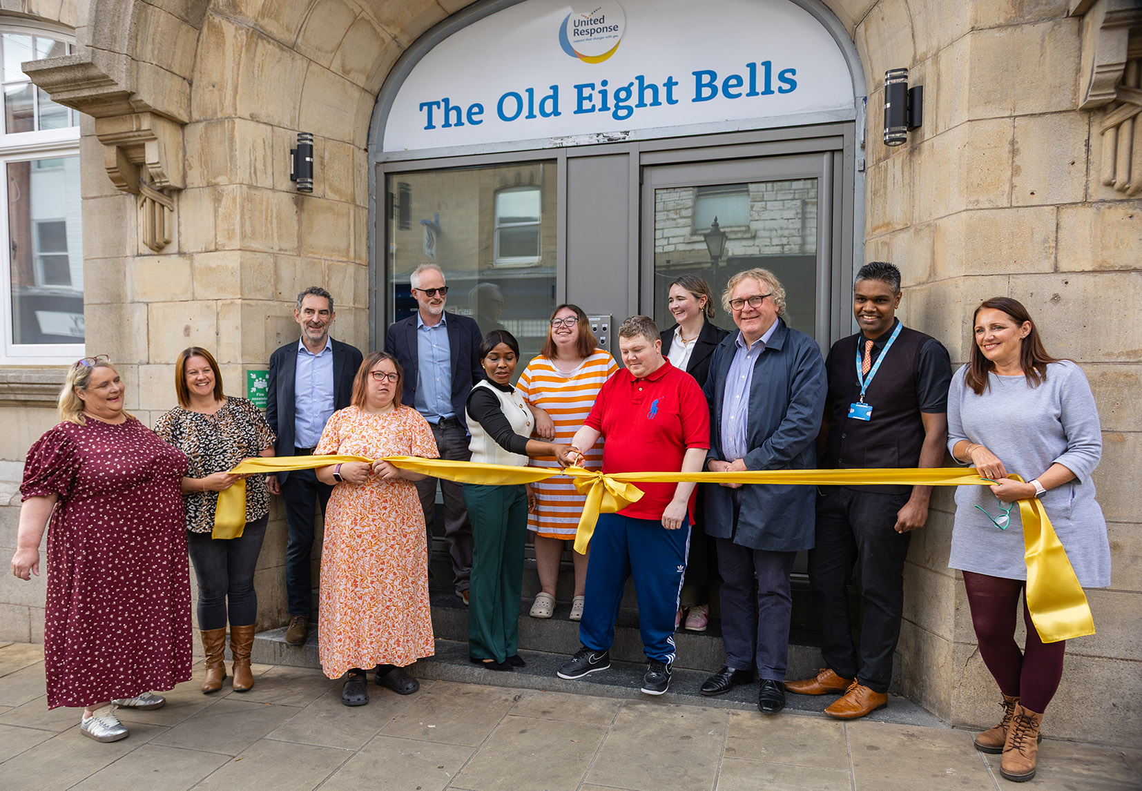 Grop of people cut a ribbon in front of a building