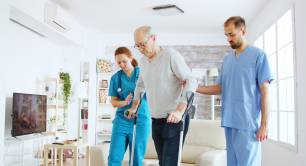 team-nurses-social-workers-helping-old-disabled-man-walk-with-his-crutches-out-nursing-home-room