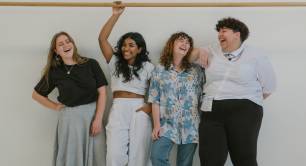 Group of four people standing in front of a white wall, laughing and smiling